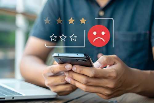 Mann bedient Smartphone, darüber negatives Smiley und schlechte Sterne Bewertung